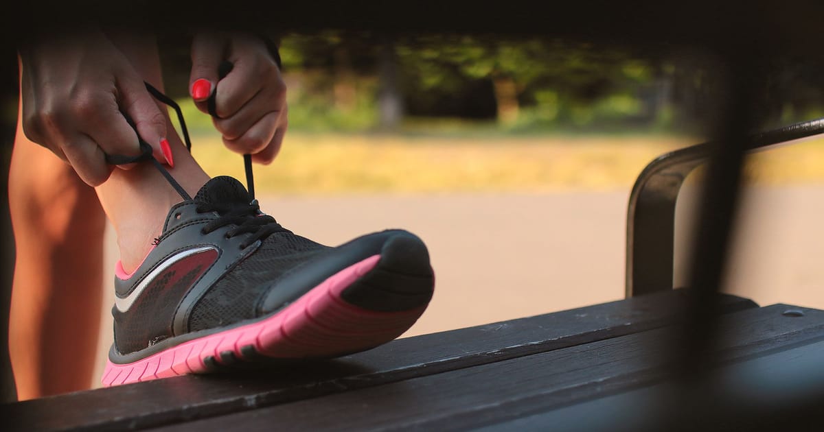 A runner lacing a road shoe on a bench, laces pulled through the top eyelet.