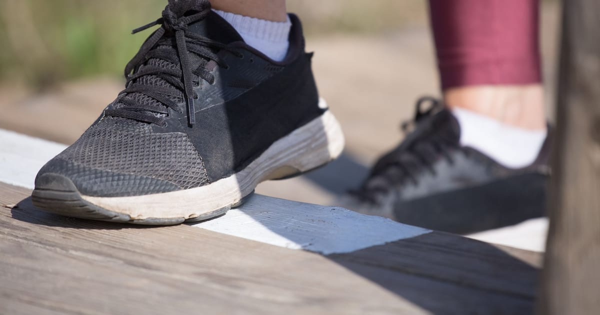 A running shoe photographed side on against a pale wall, midsole in profile.