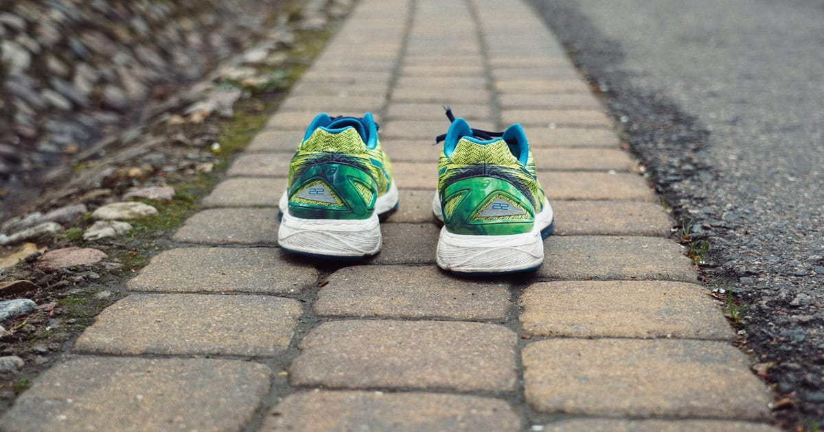 Two road running shoes side by side on wet tarmac in early morning light.