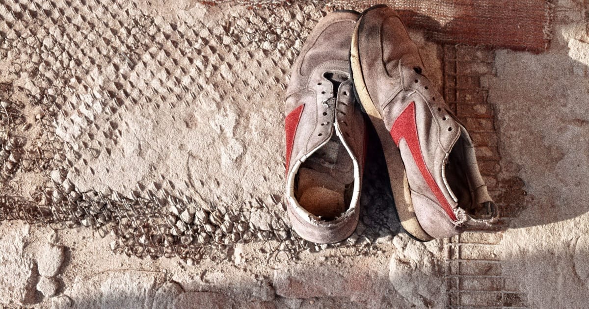 A pair of well-used road running shoes seen from the side, midsole creased and outsole worn smooth at the heel.